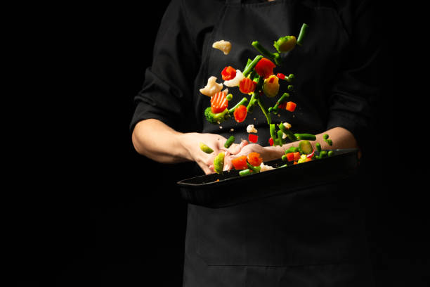 istock Professional cook. He prepares a dish with vegetables in a saucepan. on black background, menu, recipe book, healthy food 1065953924