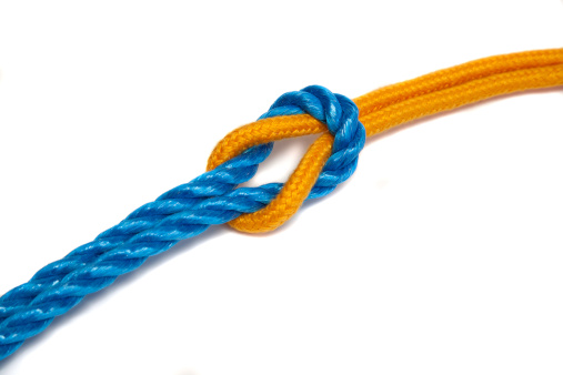 Multicolored rope with three knots on a blue background. Strong yellow-red rope with knots in the center of a blue background with free space for advertising or text