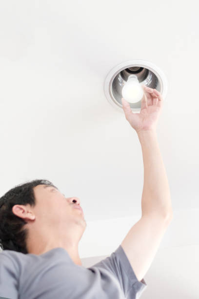 istock Power saving concept. Asia man changing compact-fluorescent (CFL) bulbs with new LED light bulb. 1065978846