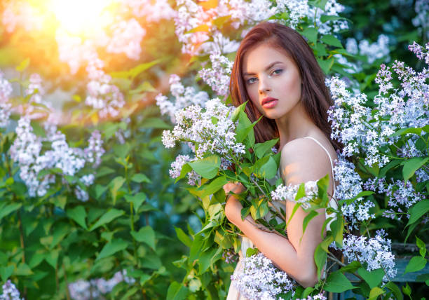 Pretty young woman posing outdoors in nature around her bush of blossoming flowers. Girl outside on a sunny summer day with white flowers. Natural flowers.