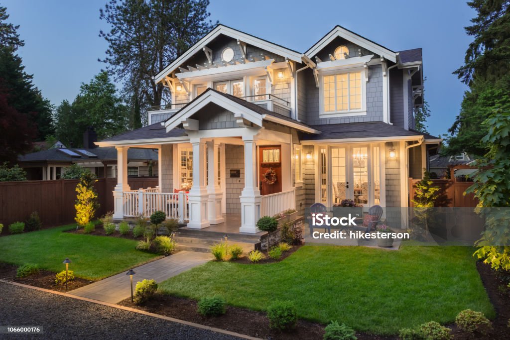 Beautiful luxury home exterior at twilight facade of home with manicured lawn, and backdrop of trees and dark blue sky House Stock Photo