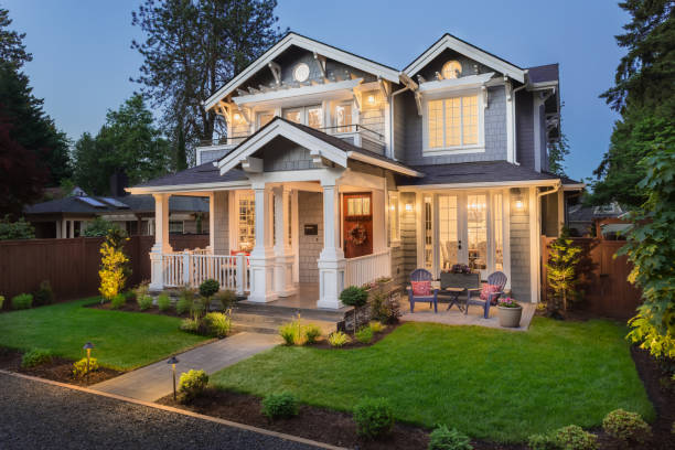 Beautiful luxury home exterior at twilight facade of home with manicured lawn, and backdrop of trees and dark blue sky model home photos stock pictures, royalty-free photos & images