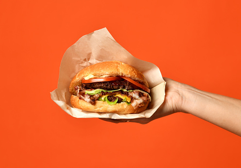 Woman hands hold big cheeseburger barbeque sandwich with marble beef on orange background
