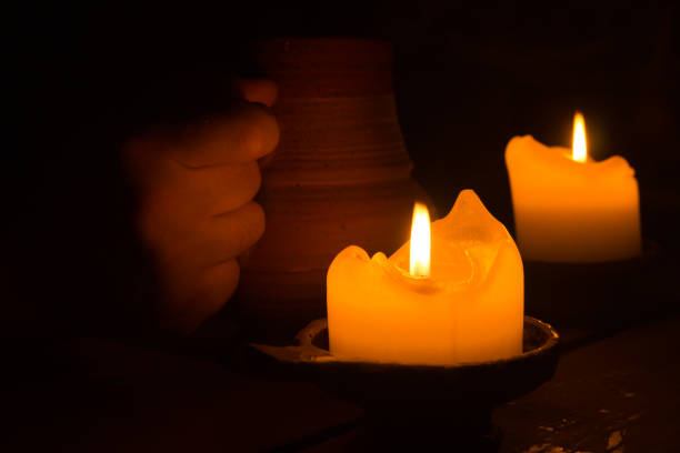 istock Two burning candles in the dark. clay mug in a hand. glowing flame 1066065346