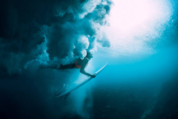 istock Surfer woman with surfboard dive underwater with under big wave. 1066088412