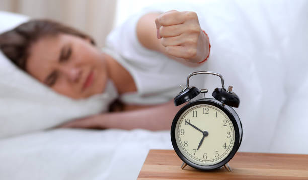 Alarm clock opposite of sleepy young woman stretching hand to ringing alarm willing turn it off. Early wake up, not getting enough sleep concept Alarm clock opposite of sleepy young woman stretching hand to ringing alarm willing turn it off. Early wake up, not getting enough sleep concept. smash alarm clock stock pictures, royalty-free photos & images