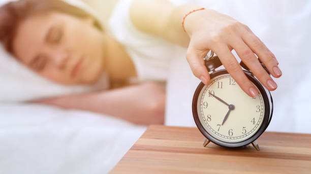 Alarm clock opposite of sleepy young woman stretching hand to ringing alarm willing turn it off. Early wake up, not getting enough sleep concept Alarm clock opposite of sleepy young woman stretching hand to ringing alarm willing turn it off. Early wake up, not getting enough sleep concept. smash alarm clock stock pictures, royalty-free photos & images