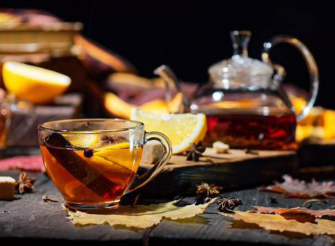 Hot black tea with fresh orange and spices on the table with autumn leaves