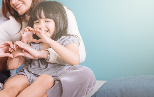 little girl making heart shape sit in mom lap.