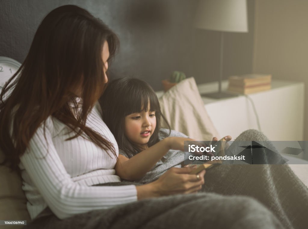 mother and daughter reading book at home in the bedroom Child Stock Photo