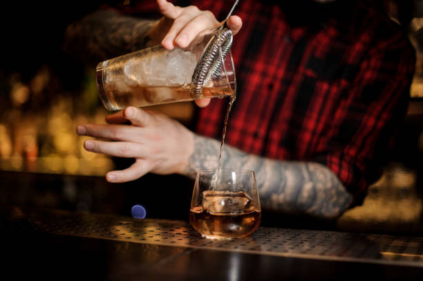 tattooed barman pouring fresh drink into a whiskey dof glass - men elegance cocktail cool imagens e fotografias de stock