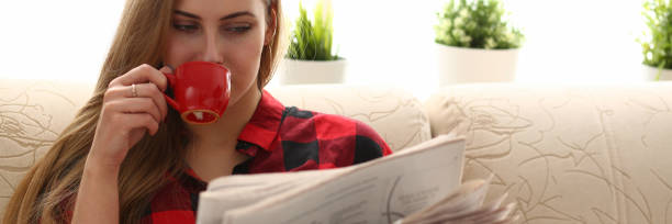 mujer bebiendo café y lectura sentado en el sofá - reading newspaper break tea fotografías e imágenes de stock