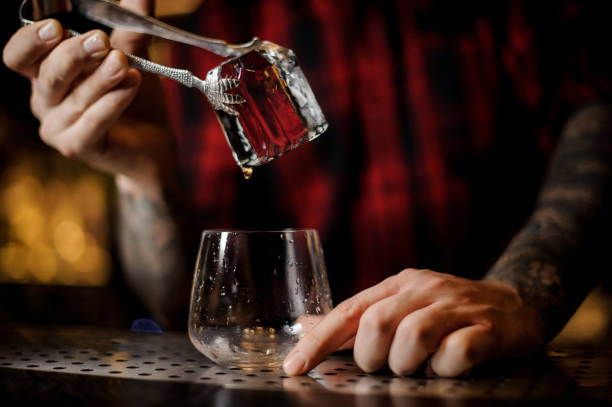 bartender hand putting a big ice cube into a whiskey dof using tongs - men elegance cocktail cool imagens e fotografias de stock