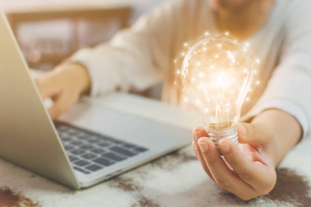 mano de mujer sosteniendo la bombilla y el uso de laptop en escritorio de madera. nueva idea de concepto con innovación y creatividad - final touch fotografías e imágenes de stock