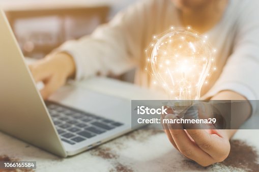 istock Woman hand holding light bulb and using laptop on wooden desk. Concept new idea with innovation and creativity 1066165584