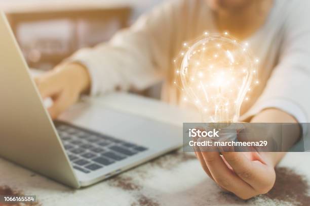 Woman Hand Holding Light Bulb And Using Laptop On Wooden Desk Concept New Idea With Innovation And Creativity Stock Photo - Download Image Now