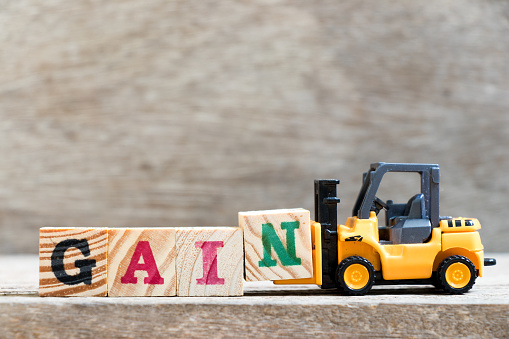 Toy forklift hold letter block N in word gain on wood background