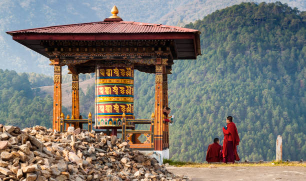 Punakha/Bhutan - March 1, 2016:  young women monks of the Buddhist monastery in their traditional red robes before classes next to the prayer wheel against the background of the Himalayan mountains Punakha/Bhutan - March 1, 2016:  young women monks of the Buddhist monastery in their traditional red robes before classes next to the prayer wheel against the background of the Himalayan mountains bhutan stock pictures, royalty-free photos & images