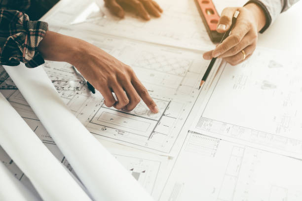 istock Close up two architect hands holding pencil and pointing on building blueprints in office room. 1066206044