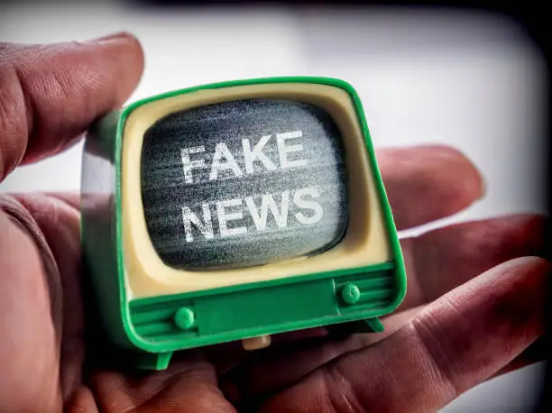 Photo of Hand holds miniature TV, fake news metaphor, conceptual image