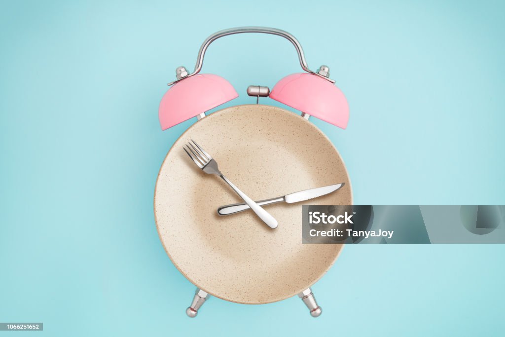 Reloj con alarma y plato con cubiertos - Foto de stock de Ayunar libre de derechos