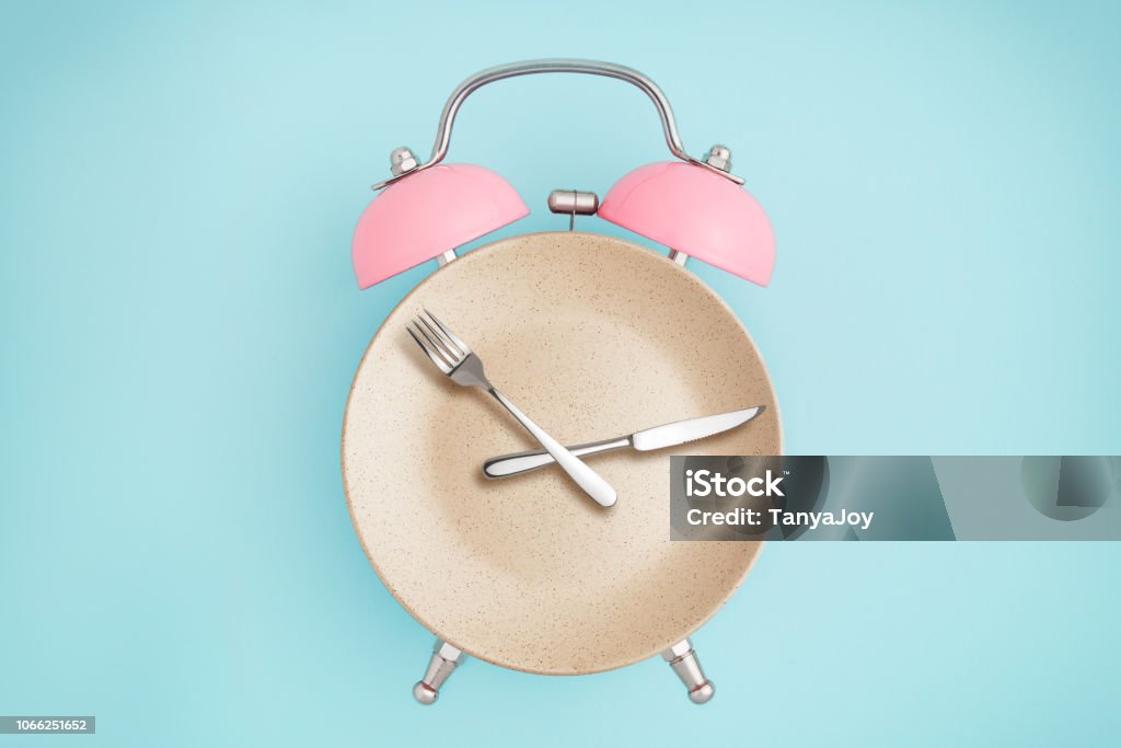 Alarm clock and plate with cutlery Alarm clock and plate with cutlery . Concept of intermittent fasting, lunchtime, diet and weight loss Intermittent Fasting Stock Photo