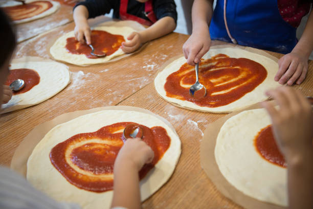 Children's hands make pizza - spread tomato sauce on the base. stock photo
