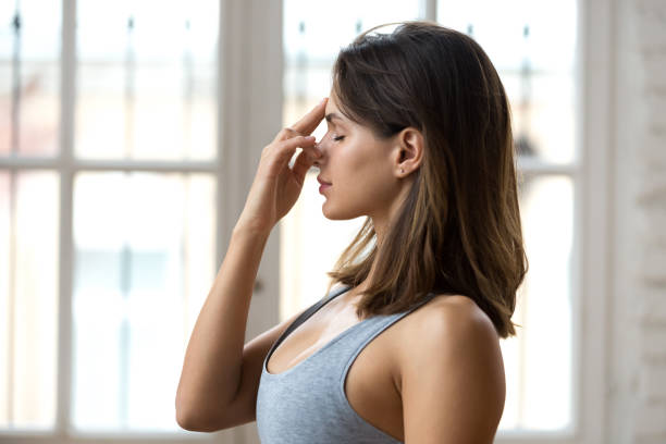 Young woman practicing yoga, nadi shodhana pranayama pose, close up Young sporty woman practicing yoga, doing Alternate Nostril Breathing exercise, nadi shodhana pranayama pose, working out, wearing sportswear, grey top, indoor close up, yoga studio, side view inhaling stock pictures, royalty-free photos & images