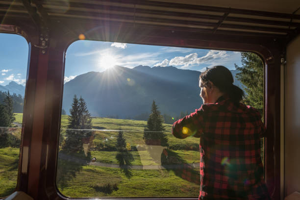 Woman looks out window of moving rail coach, on railway Mountains in distance, Bernese Oberland train interior stock pictures, royalty-free photos & images