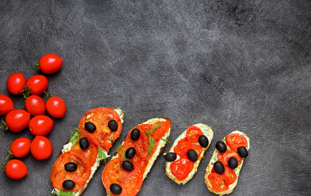 Black bread with cheese and fried tomatoes. Flat lay, top view, copy space. Italian brochettes on a platter. Red tomatoes and black olives on black stone background.