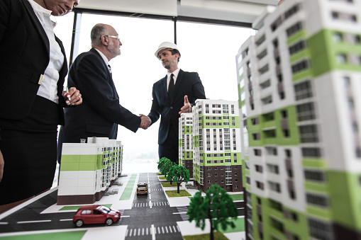 Business people standing near residential quarter houses models and shaking hands, meeting of architects and investors