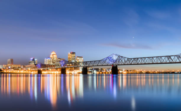 Louisville Skyline and Ohio River Bridget at Night A long-exposure of the Louisville, Kentucky skyline taken from the Indiana bank of the Ohio River at blue-hour, including the 2nd street bridge and reflected city lights on the water in the foreground and the crescent moon above the bridge. ohio river photos stock pictures, royalty-free photos & images