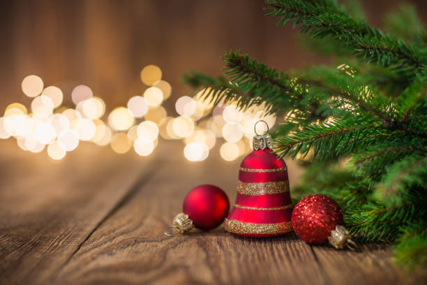 Fir twig and red bell bauble on rustic wood and sparkles light backgorund Fir twig and red bell bauble on rustic wood and sparkles light backgorund red backgorund stock pictures, royalty-free photos & images