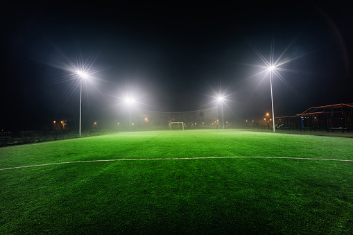 Illuminated football playground with green grass, modern football goal net and lens flares on background.