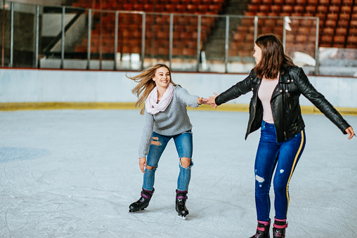 Teenage girls having fun at ice skating rink together during winter holidays