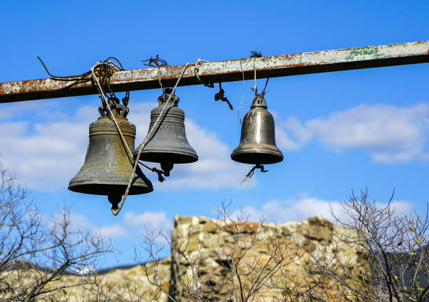 Ancient stone bell tower with two bronze bells and a tiled roof stands against a clear blue sky, showcasing rustic architecture and historical charm in rural Spain