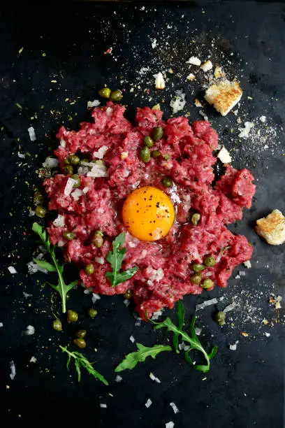 Beef tartare on a black slate or metal background- traditional dish of french cuisine.Top view.