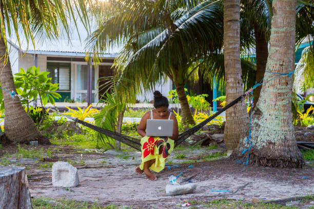 Young Polynesian woman in a hammock with a notebook working outdoors under palm trees. Tuvalu, Polynesia, Oceania. .tv domain concept illustration. stock photo