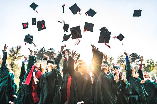 Graduation day! Large group of happy college students celebrating their graduation day outdoors while throwing their caps up in the air. college life stock pictures, royalty-free photos & images