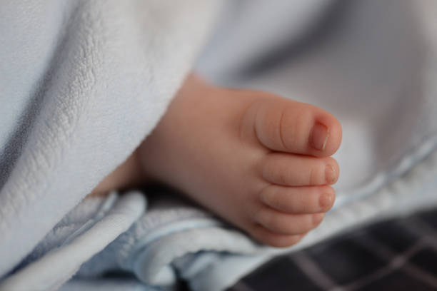 Tender little baby's foot under a blue blanket.
