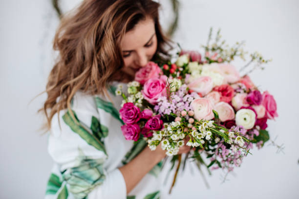 Florist makes a bouquet. A girl florist makes a bouquet in a light studio on a wooden table. flowering plant stock pictures, royalty-free photos & images