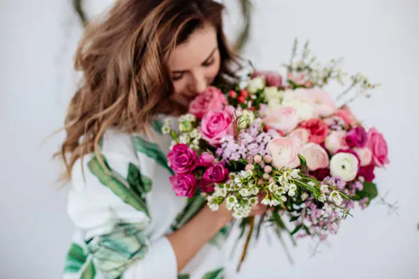 A girl florist makes a bouquet in a light studio on a wooden table.