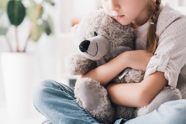 cropped shot of depressed little child embracing her teddy bear stock photo