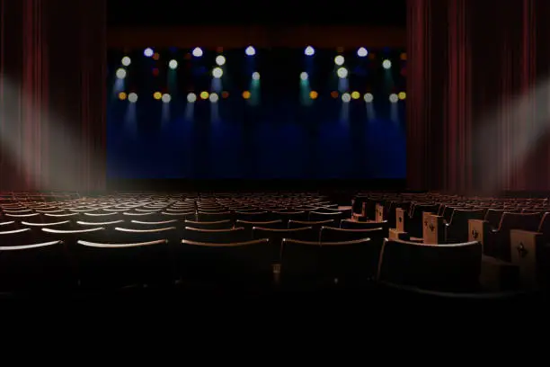 Photo of empty seat in vintage auditorium or theater with lights on stage.