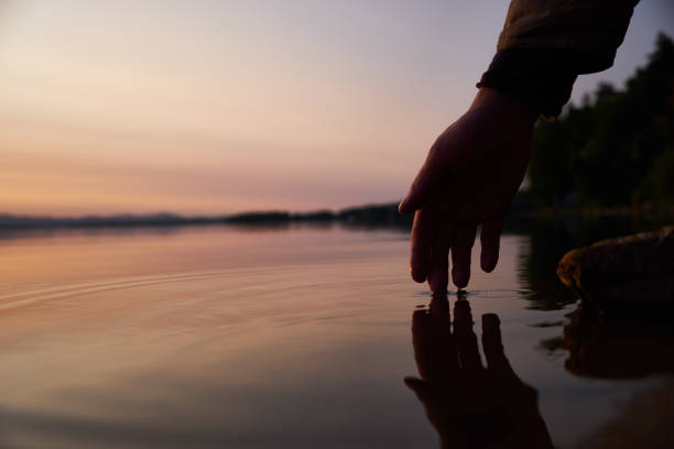 Human hand touching the fresh water from lake stock photo
