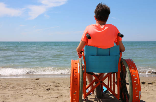 boy on the special wheelchair with metal wheels on the beach - esclerose lateral amiotrófica imagens e fotografias de stock