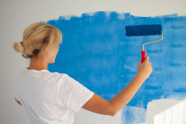 istock woman painting a wall with paint roller 1066487346