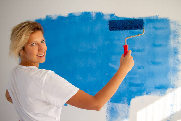istock woman painting a wall with paint roller 1066487378