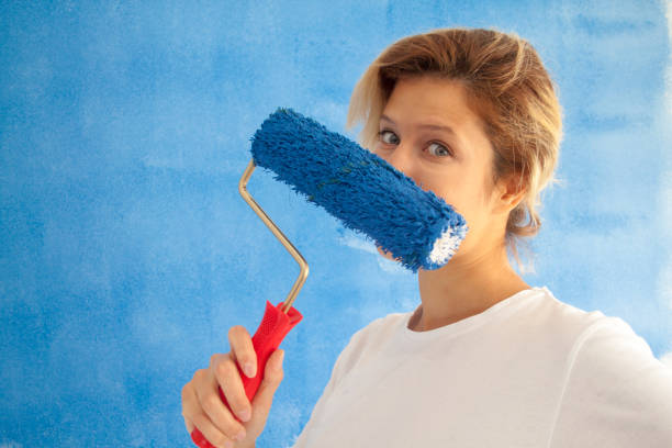 istock woman painting a wall with paint roller 1066487392