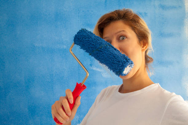 istock woman painting a wall with paint roller 1066487396
